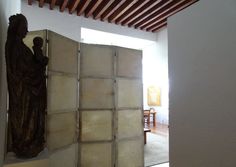 an open door leading to a statue in a room with white walls and wood beams