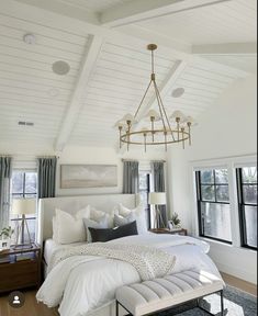 a large white bed sitting under a chandelier in a bedroom next to two windows