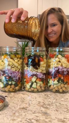 a woman pours dressing into jars filled with vegetables and beans to make pasta salad