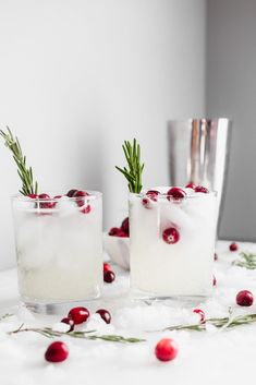 two glasses filled with ice, cranberries and rosemary sprigs on the table