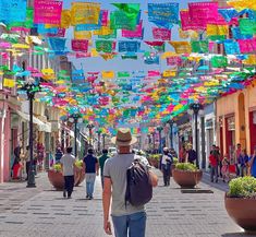 a man walking down a street with lots of colorful flags hanging from it's ceiling