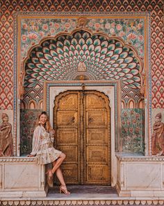 a woman posing in front of an ornate doorway with intricate carvings on the walls and doors