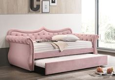 a pink daybed sitting on top of a hard wood floor next to a window