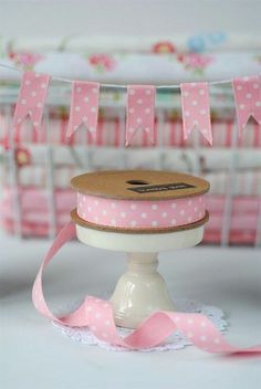 a pink and white polka dot ribbon on top of a cake stand with ribbons hanging from it