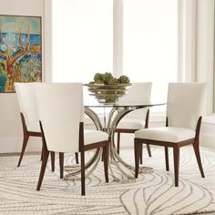 a glass dining table with white chairs and a bowl of fruit on top of it