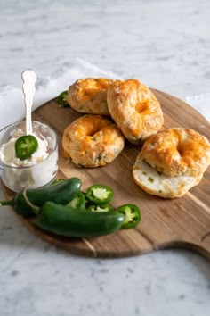 several bagels on a wooden cutting board with cream and jalapeno peppers