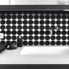 a bathroom sink with black and white tiles on the wall behind it, along with other accessories