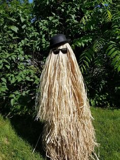 a man with long hair wearing a hat and glasses is standing in the grass next to some bushes