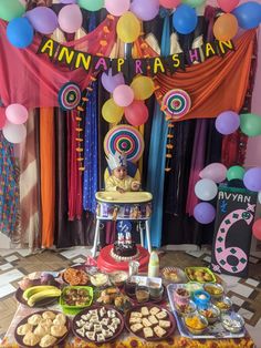 an assortment of desserts and snacks on a table in front of a backdrop with balloons