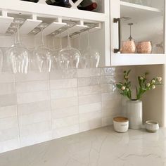 a kitchen counter with wine glasses on the shelf and flowers in vases next to it