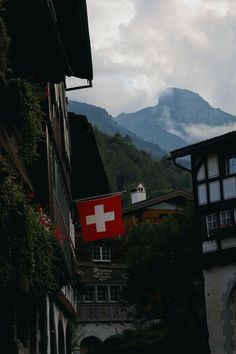 a swiss flag is hanging on the side of an old building with mountains in the background