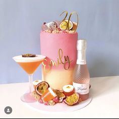 there is a pink cake with gold lettering on it and two glasses next to it