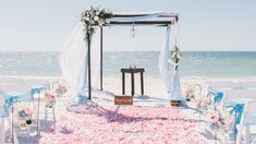 an outdoor wedding setup on the beach with blue and white chairs, pink flowers and petals