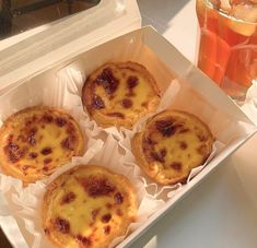 four small pastries in a white box next to a glass of tea and an orange juice