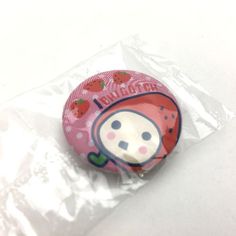 a pink button with strawberrys on it sitting in a plastic wrapper next to a white surface