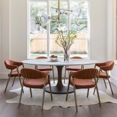 a dining room table with four chairs and a vase on it in front of a large window