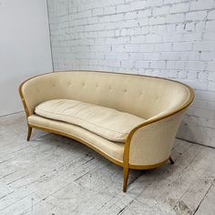 a beige couch sitting on top of a wooden floor next to a white brick wall