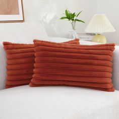 two orange pillows sitting on top of a white couch next to a vase with flowers