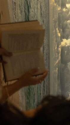 a person reading a book in front of a window with the ocean and sky behind them