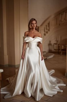 a woman in a white wedding dress standing on the floor with her arms behind her back