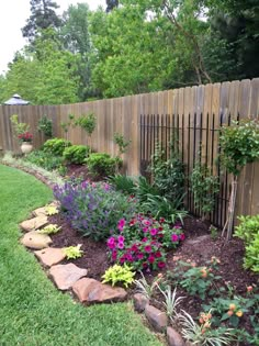 a garden with flowers and rocks in the grass next to a wooden fence that is surrounded by green grass