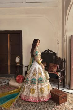 a woman in a white and gold wedding dress standing next to a chair with luggage