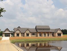 a large house sitting on top of a lush green field next to a lake in front of it