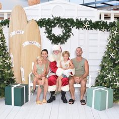 a family sitting on a bench in front of christmas decorations and surfboards with santa