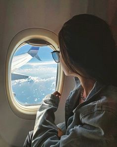 a woman looking out an airplane window at the clouds