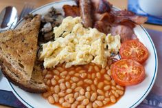 a white plate topped with eggs, beans and toast next to tomatoes on a table