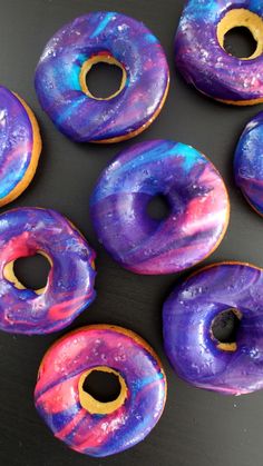 there are many donuts with purple and blue icing on them, all together