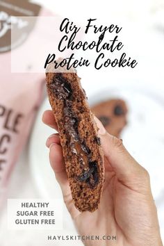 a person holding a chocolate protein cookie in their hand with text overlay that reads, air fryer chocolate protein cookie healthy sugar free gluft