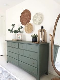 a green dresser sitting in front of a mirror next to a wall with pictures on it