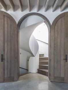 an open door leading to a spiral staircase in a white walled room with wooden doors