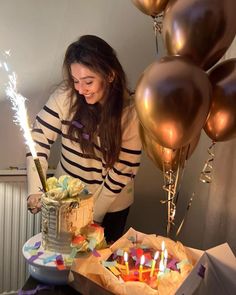 a woman standing in front of a cake with lit candles on it and balloons behind her