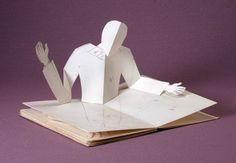 an open book with paper cut out of the shape of a person sitting on it