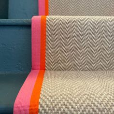 an orange and pink striped rug sitting on top of a blue stair case next to a wall