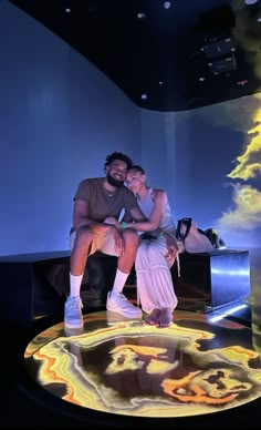 a man and woman sitting on top of a table in front of a projection screen