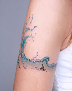 a woman's arm with a wave tattoo on it and a sailboat in the water