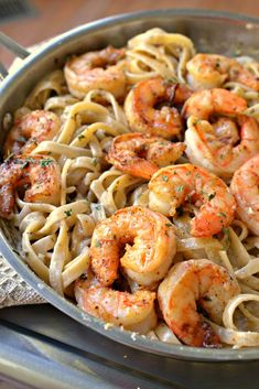 shrimp and pasta in a skillet on top of a wooden table with a napkin