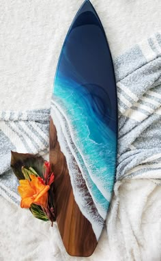 a surfboard is laying on the beach towel next to an orange flower and some towels