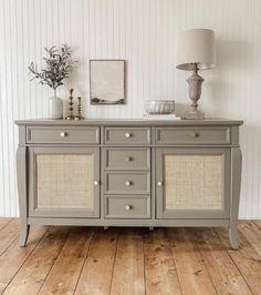 the sideboard is painted gray with wicker doors and drawers, along with a lamp