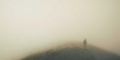 a lone person standing on top of a hill in the middle of foggy weather