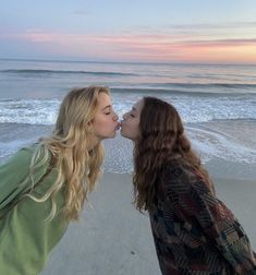 two women kissing each other on the beach at sunset with waves crashing in behind them