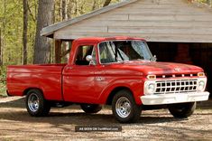 an old red pick up truck parked in front of a wooden building with a roof