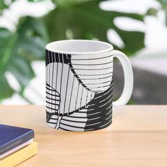 a black and white coffee mug sitting on top of a wooden table next to a book