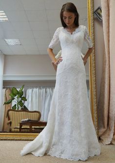 a woman standing in front of a mirror wearing a white wedding dress with short sleeves