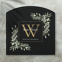 a black and gold monogrammed sign with greenery on the front reads whitney