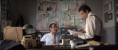 two men sitting at a desk in an office