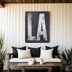 a white couch sitting under a large black and white sign next to potted plants